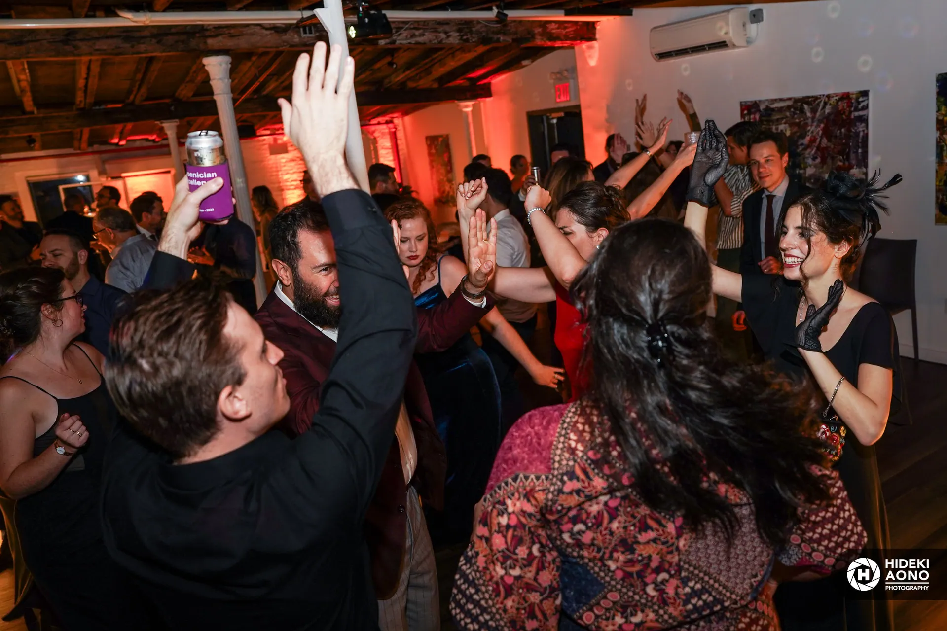 A company party dance floor under red uplighting, guests dancing with hands up